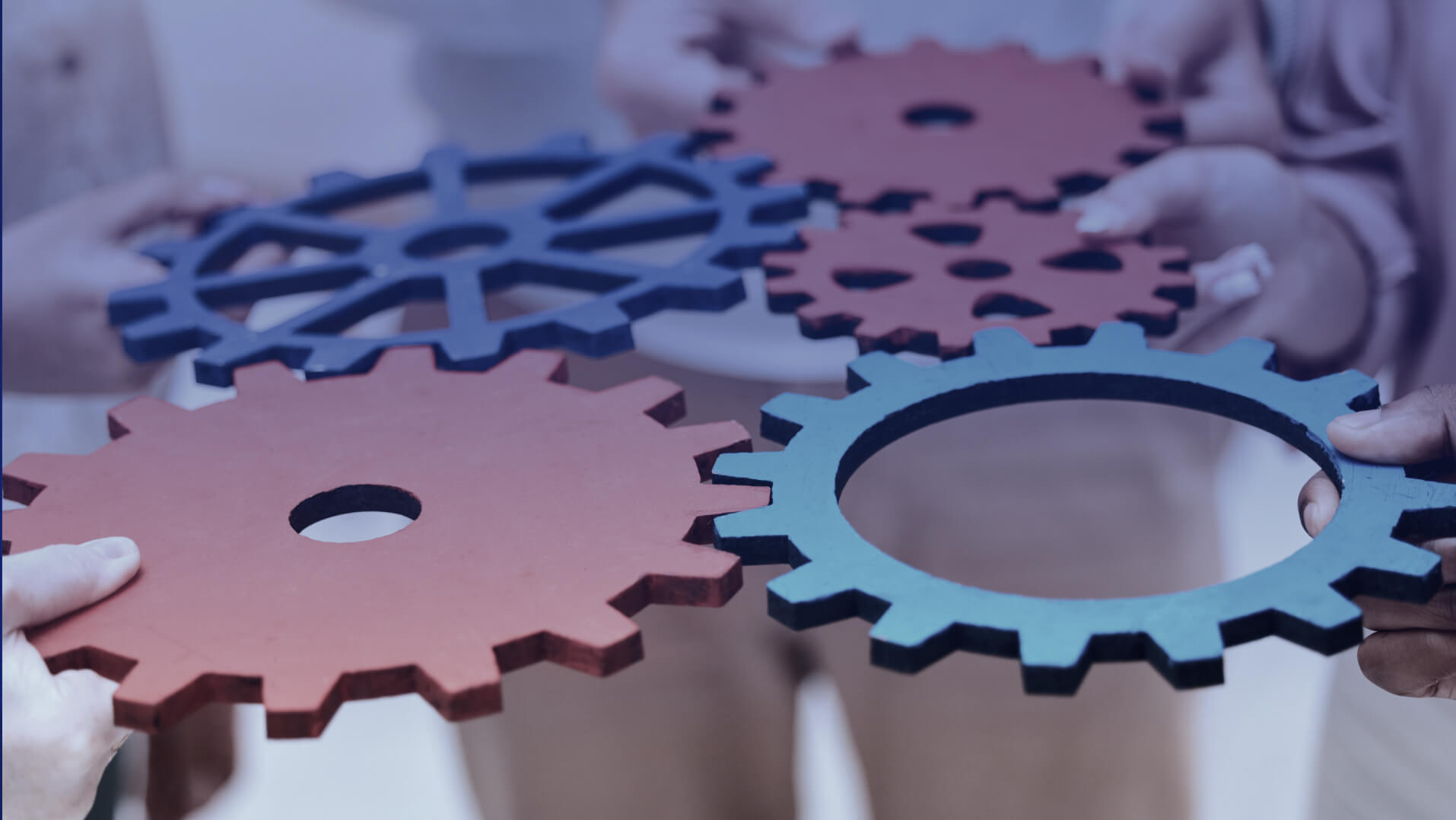 Rouages de différentes tailles et couleurs tenus par des personnes, pour faire fonctionner un système